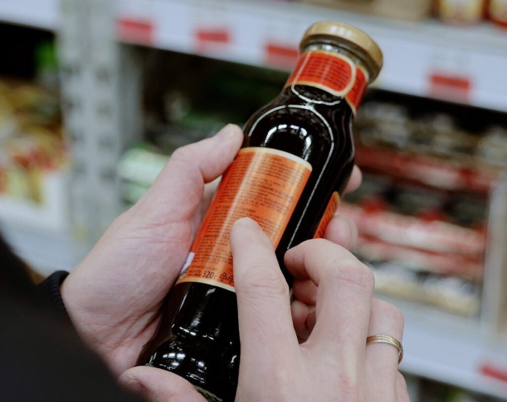 a person scanning the ingredients label on a bottle of dark sauce.