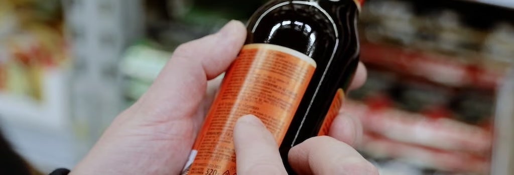 a person scanning the ingredients label on a bottle of dark sauce.