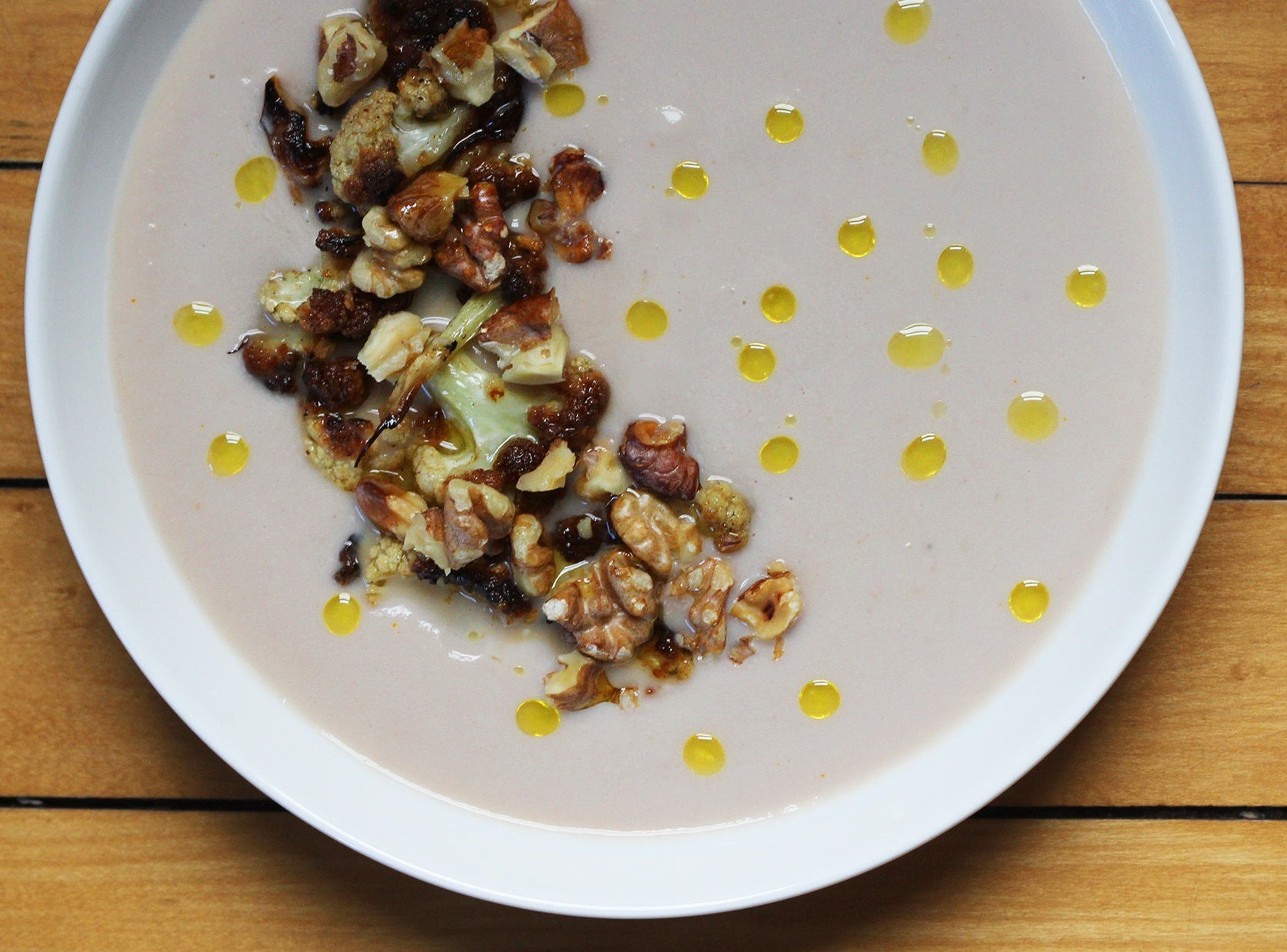 A bowl of creamy cauliflower soup topped with roasted cauliflower and toasted walnuts and drips of extra virgin olive oil