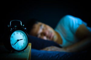 man sleeping in a bed at night with an alarm clock in the foreground showing the time as three am