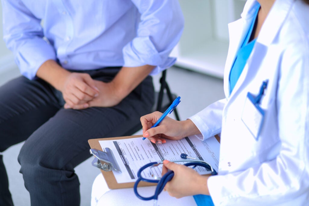 Doctor with a stethoscope and a clipboard sitting and talking to a patient